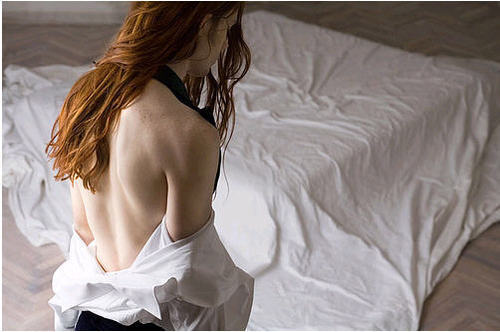 Wearing his shirt pushed down to his waist, a man stands before a bed. His head is bowed and his long red hair is pulled over one shoulder.This photograph was suggested by Madam Harkonnen, who wrote:I get a strong sense of narrative in this light, poised photograph: the cloth tangling his arms in a suggestion of things to come; his hair just brushed aside to bare his shoulder for someone, and long enough to wrap around his neck.  Now he’s just waiting with elegant composure for a word or a touch…waiting for the storm to break over him.This picture strikes me as almost more angelic than most images depicting angels do. The white light, clothing, and bed linens set a simple but, in the absence of much else, surreal tone. However, it&#8217;s the model that carries the image.The man&#8217;s hair is especially worthy of note because, while I think its length is beautiful on him, it&#8217;s also transgressive. In some religions, long hair is often thought to be appropriate only for women, as this Christianity-inspired article showcases, saying that Men should look like men, and women should look like women. God is not interested in, nor does He accept, &#8220;unisex.&#8221; While god may not be interested in gender presentation, I am, because not all cultures, or religions, agree on what is manly or womanly. Moreover, as gender isn&#8217;t a dichotomy, it&#8217;s very possible to mix gender signals of one kind with signals of another, resulting in additive gender.-maymay